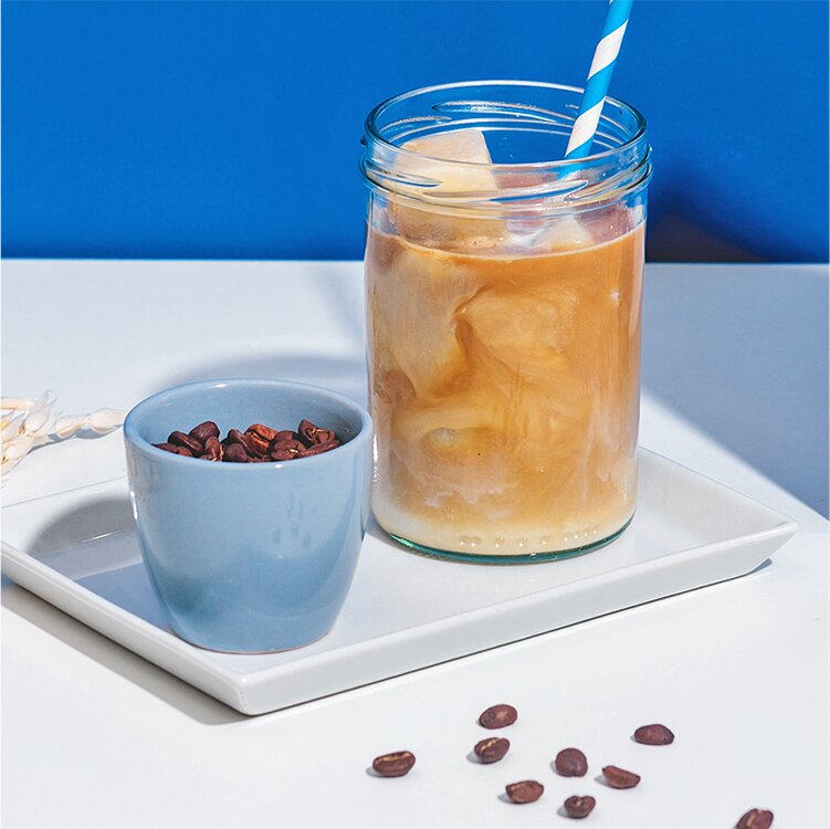 Eiskaffee mit Haferdrink Eiswürfeln und eine Tasse mit Kaffeebohnen daneben