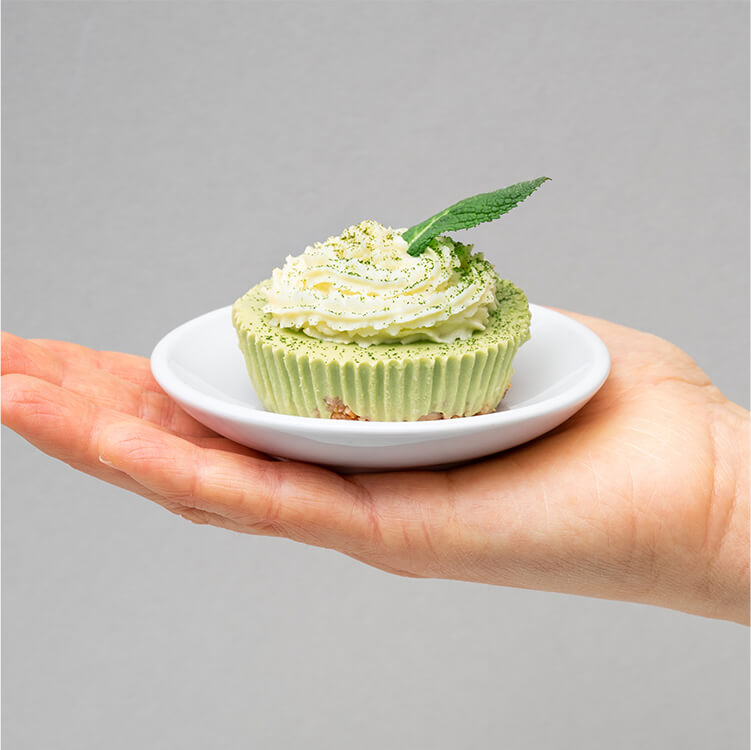 Matcha Cheesecake auf einem kleinen Teller auf einer Hand