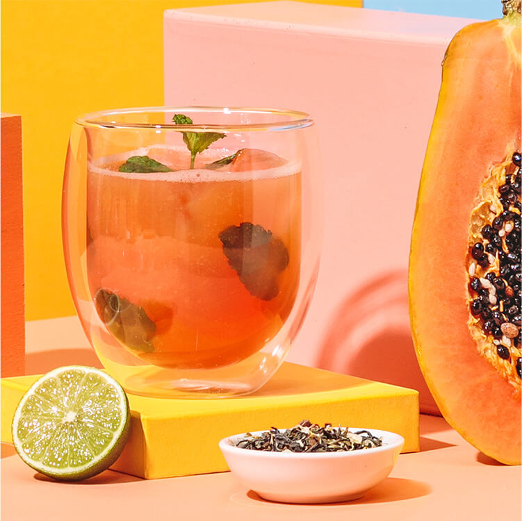 Papaya Eistee mit einer halben Papaya, Limette und Tee daneben