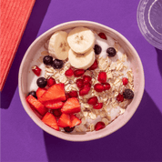 mymuesli Bio Fit in Shape Superfruit Müsli in Schale mit Milch sowie frischen Bananen, Erdbeeren und Granatapfelkernen