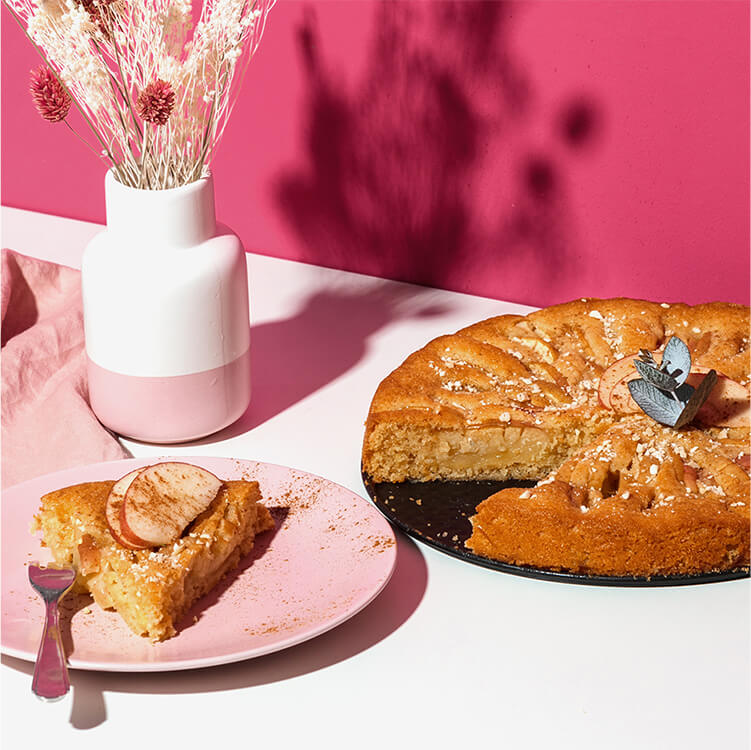 Apfelkuchen in einer Springform und daneben ein Teller mit einem Kuchenstück