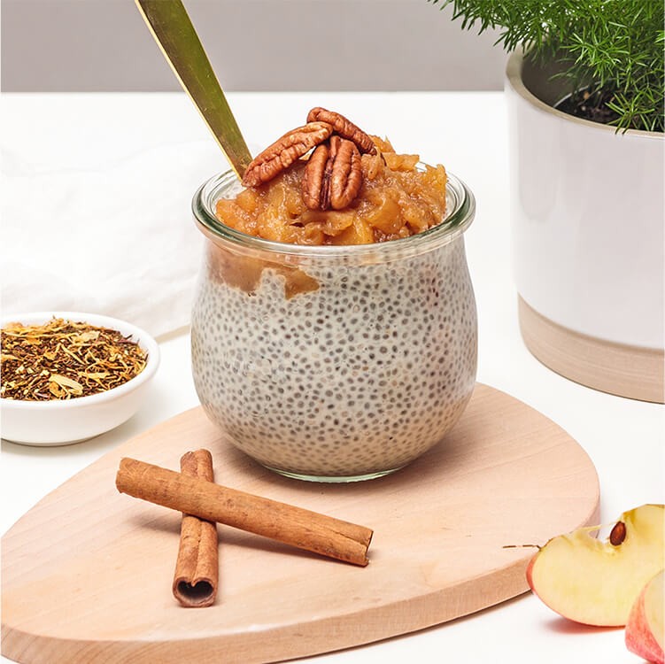 Chiapudding mit Nüssen dekoriert und daneben Apfelspalten und Zimtstangen