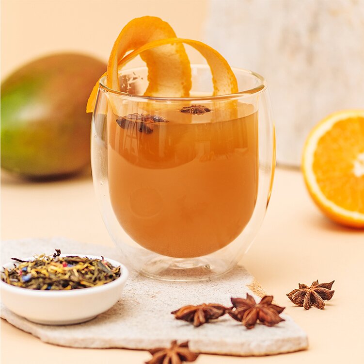 Sencha Mango Punsch im Glas mit Gewürzen und einer halben Orange