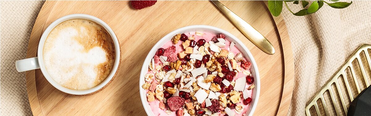 Breakfast Smoothie Bowl auf einem Tablett mit einem Kaffee und goldenen Löffel daneben