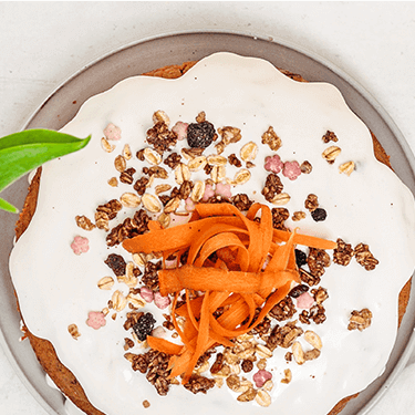 Naked Carrot Cake auf einem Teller, mit geraspelter Möhre dekoriert