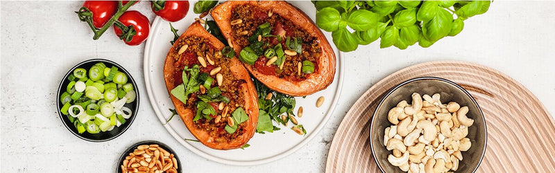 Tomate-Brokkoli-Süßkartoffel auf einem Teller, daneben Schüsseln mit Cashews, Tomaten und Lauchzwiebeln