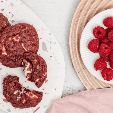 Red Velvet Cookies auf einem Teller und Himbeeren daneben