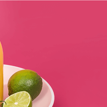 Mango Smoothie in einer Flasche und daneben Bananenscheiben und Limetten