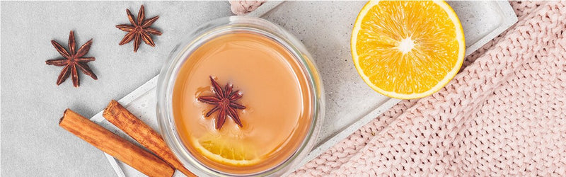 Glory's Chai Punsch in einem Glas mit Gewürzen und einer halben Orange