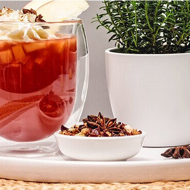 Bratapfel Punsch mit Zimtsahne, mit einem Apfel, Pflaumen, Tee und Gewürzen daneben