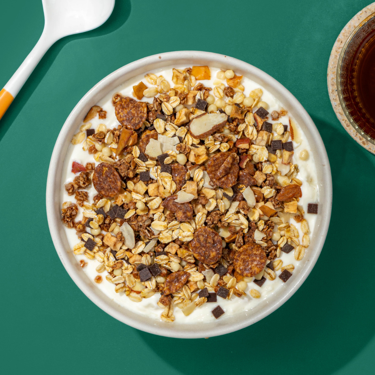 Eine Müsli-Bowl mit hellem Joghurt und einer Mischung aus Nüssen und Getreideflocken auf einem dunkelgrünen Untergrund.