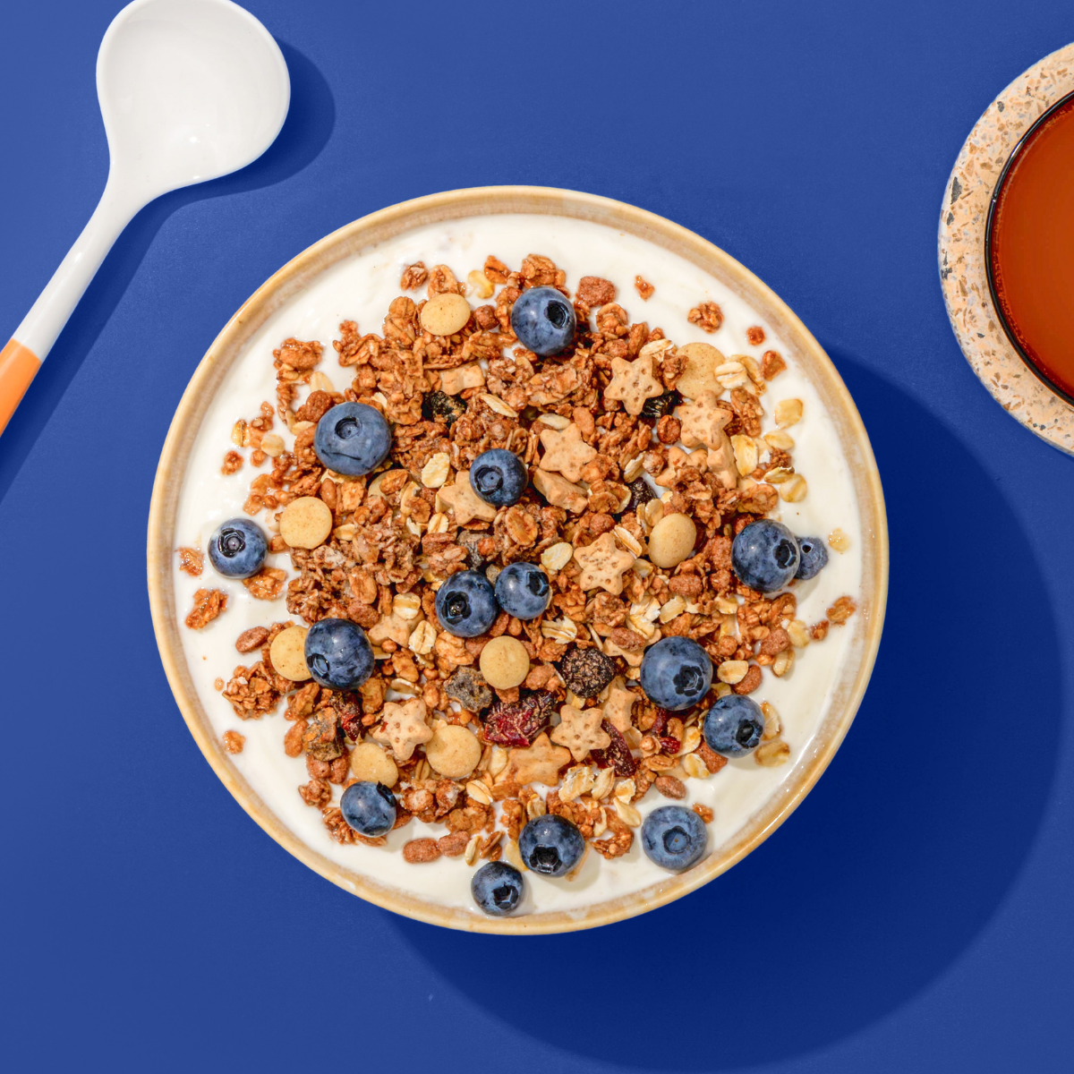 Müsli mit Chrunchy Müsli, Blaubeeren und Haferflocken in Müsli Schale, daneben ein Löffel und eine Tasse Kaffee