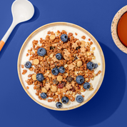 Müsli mit Chrunchy Müsli, Blaubeeren und Haferflocken in Müsli Schale, daneben ein Löffel und eine Tasse Kaffee