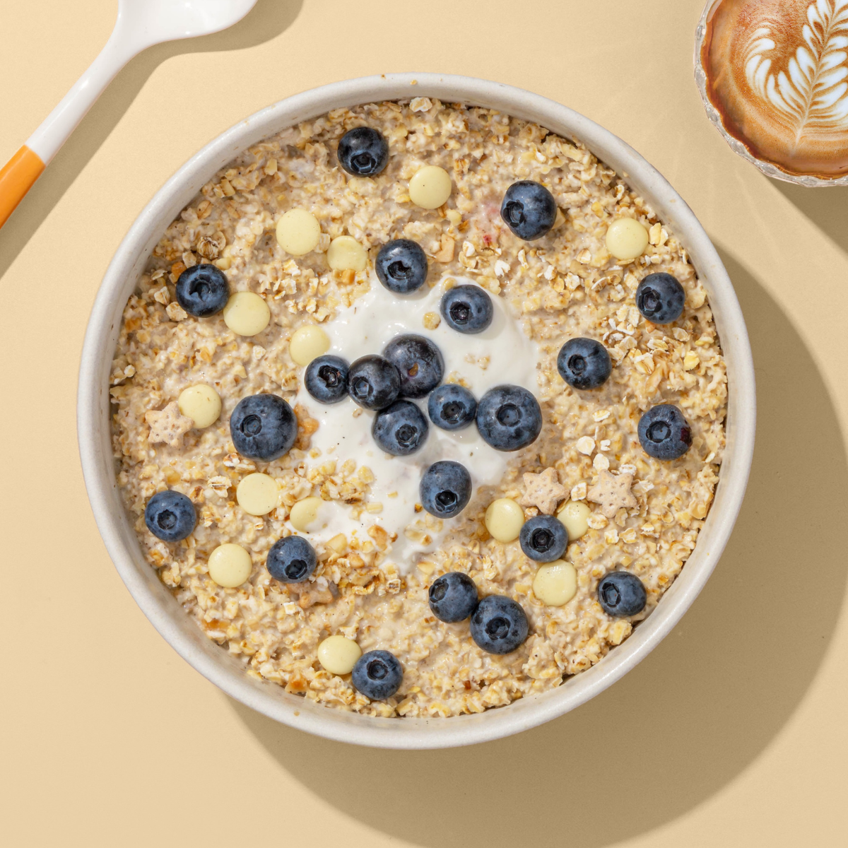 Müsli-Schale mit Blaubeeren und weißen Schokoperlen auf beigem Hintergrund.