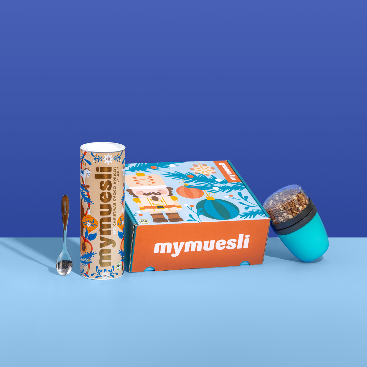 Das mymuesli Geschenkset, bestehend aus Bio Christmas Choco Apricot Crunch, Müsli 2go Becher in türkis und einem silbernen mymuesli Löffel. Verpackt in einer weihnachtlichen Geschenkbox. 