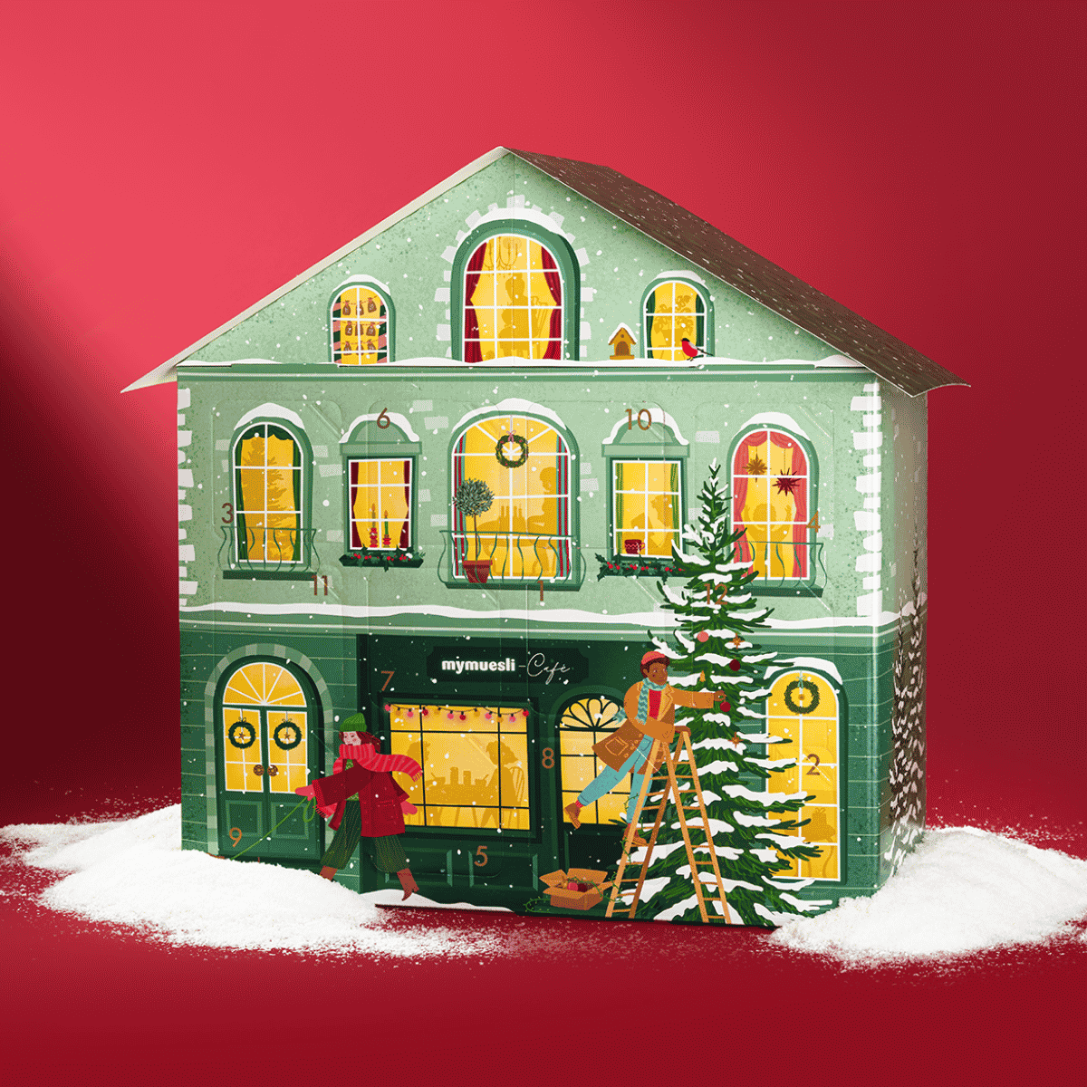 Grünes Adventskalenderhaus mit leichtem Schnee. Vor dem Haus läuft eine Frau mit ihrem Dackel vorbei. Ein Mann steht auf der Leiter und schmückt einen Tannenbaum. Die Fenster des Hauses sind beleuchtet. 