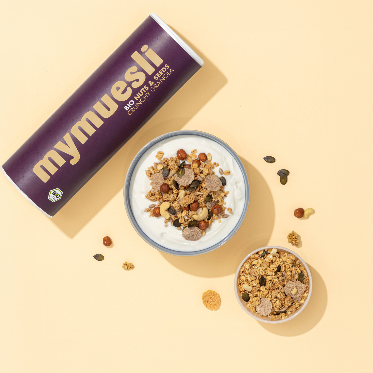 mymuesli Bio Nuts & Seeds Crunchy Granola Dose. Daneben ist eine zubereite Schale mit dem Nuts & Seeds Müsli und weißem Joghurt.