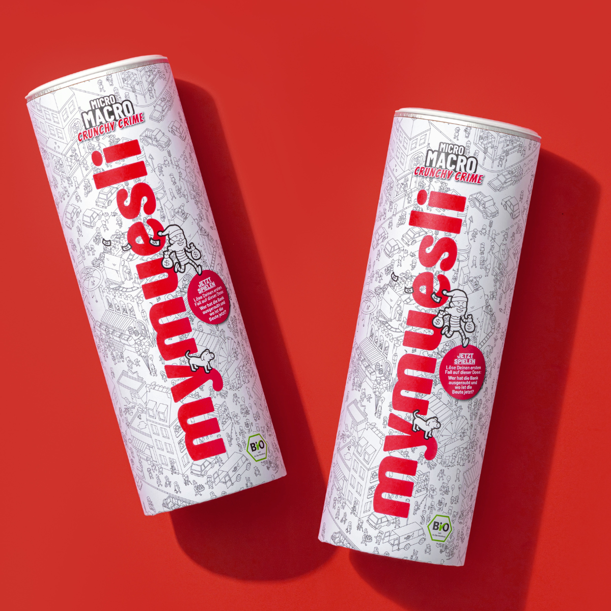 Produktabbildung zwei nebeneinander liegenden mymuesli Micro Macro Crunchy Crime Müslidosen. 