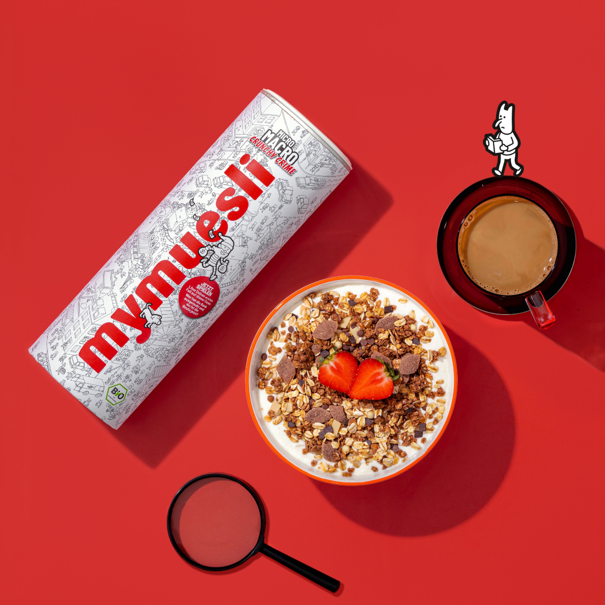 Das angerichtete mymuesli Micro Macro Crunchy Crime Müsli mit frischen Erdbeeren. Links daneben die mymuesli Micro Macro Crunchy Crime Müslidose, eine Lupe sowie ein frischer Kaffee. Auf roten Hintergund und mit einer Illustration versehen. 