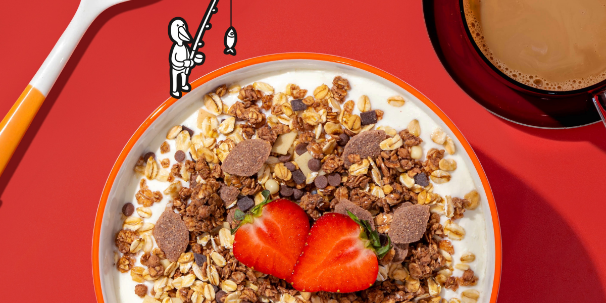 Eine angeschnittene Müslischale mit dem mymuelsi Micro Macro: Crime City Müsli. Die Sorte Super Choc mit frischen Erdbeeren. Auf rotem Hintergrund. 