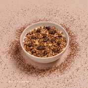 Eine Schüssel mit Tiramisu Müsli und schokolierten Espressobohnen, umgeben von Kakaopuder auf einem hellbraunen Untergrund.