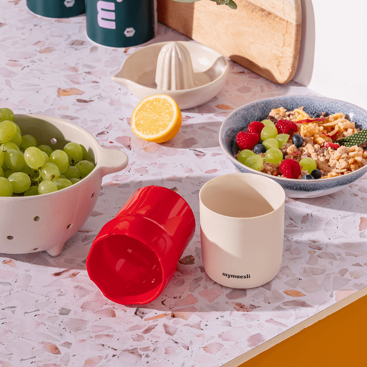 Apfelreibe mymuesli und dahinter eine Schüssel Bircher mit geriebenem Apfel, Weintrauben und Beeren