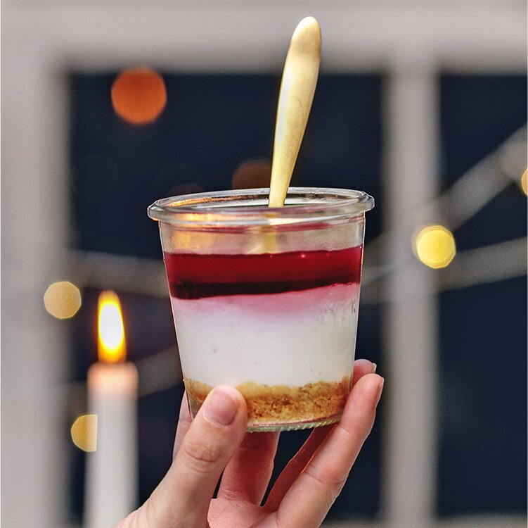 Cheesecake im Glas mit Tee-Topping und goldenem Löffel in der Hand