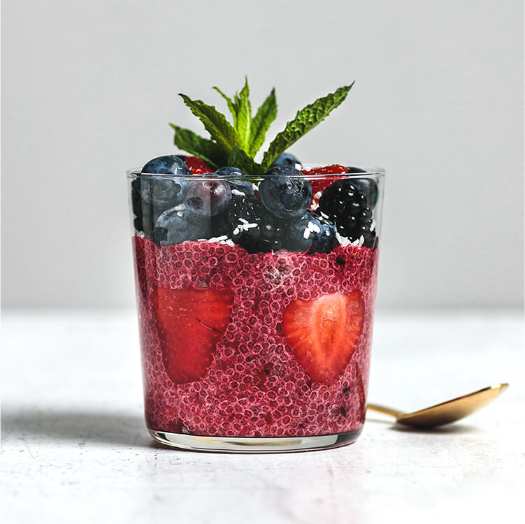 Chia Kokos Pudding mit Beeren im Glas mit einem goldenen Löffel daneben