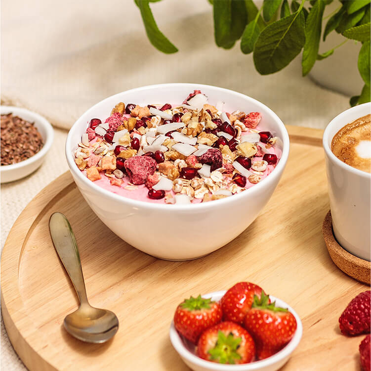 Breakfast Smoothie Bowl auf einem Tablett mit einem Kaffee, Erdbeeren und goldenen Löffel daneben