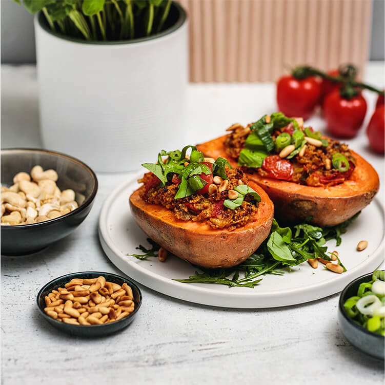Tomate-Brokkoli-Süßkartoffel auf einem Teller, daneben Schüsseln mit Cashews, Tomaten und Lauchzwiebeln