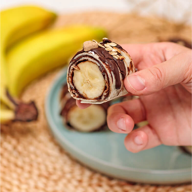 Schoko Bananen Sushi auf einem Teller mit Banane dahinter
