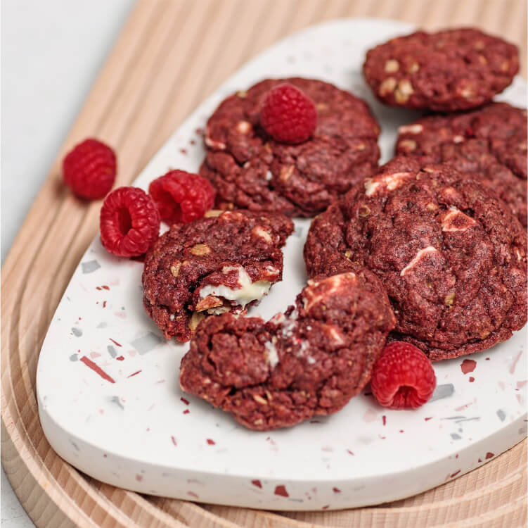 Red Velvet Cookies auf einem Teller und Himbeeren daneben