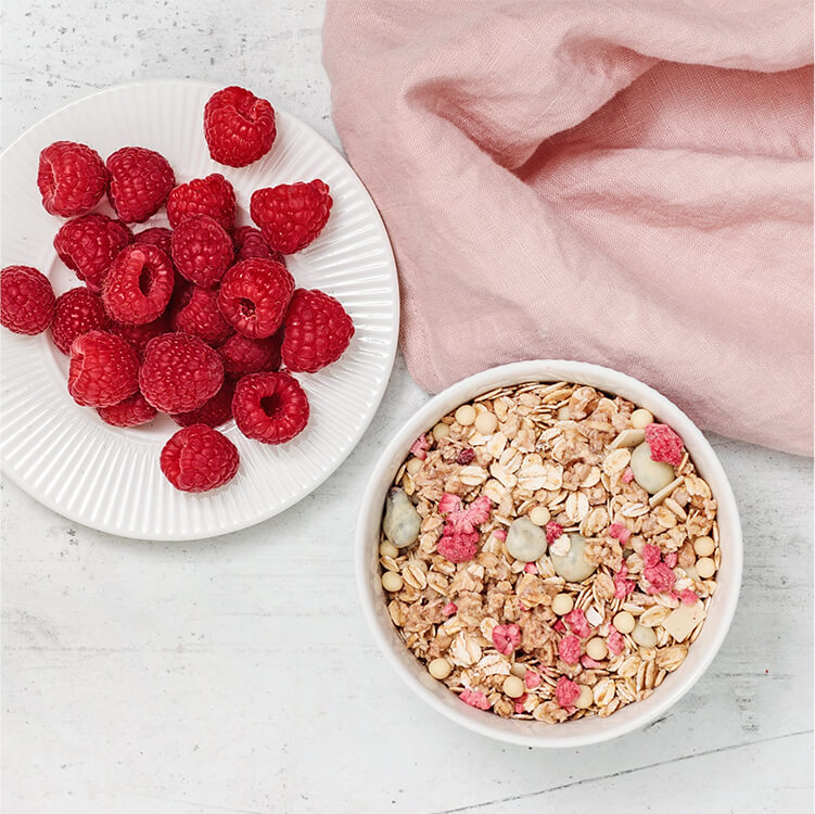 Himbeeren und daneben eine Schale mit Berry White Choc Müsli