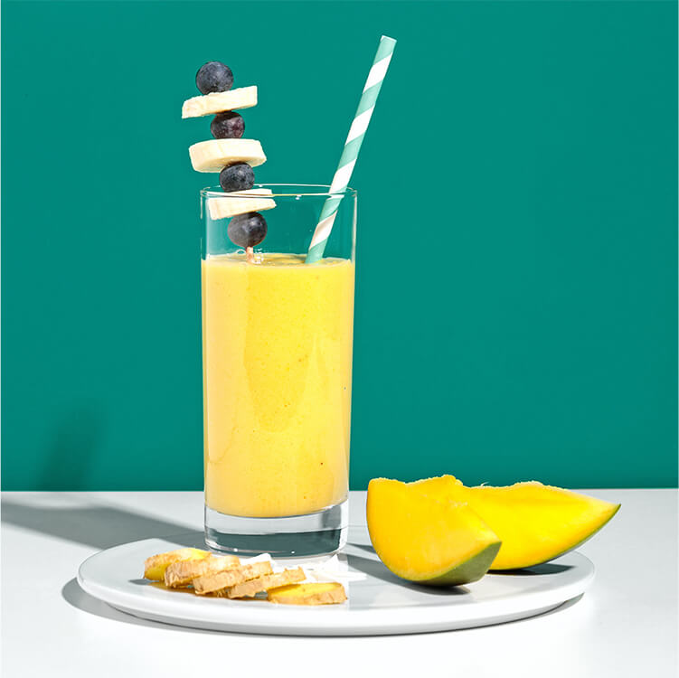 Bananen Smoothie mit einem Strohhalm auf einem Teller mit Mango und Ingwer