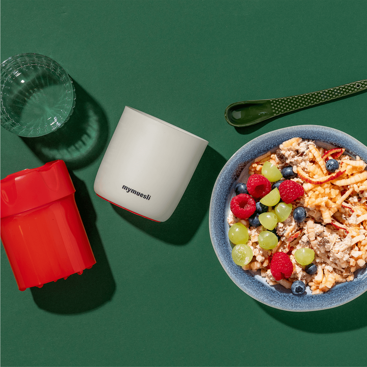 mymuesli Apfelreibe neben Schale mit Bio Bircher Müsli mit frischen Himbeeren, Blaubeeren und Trauben