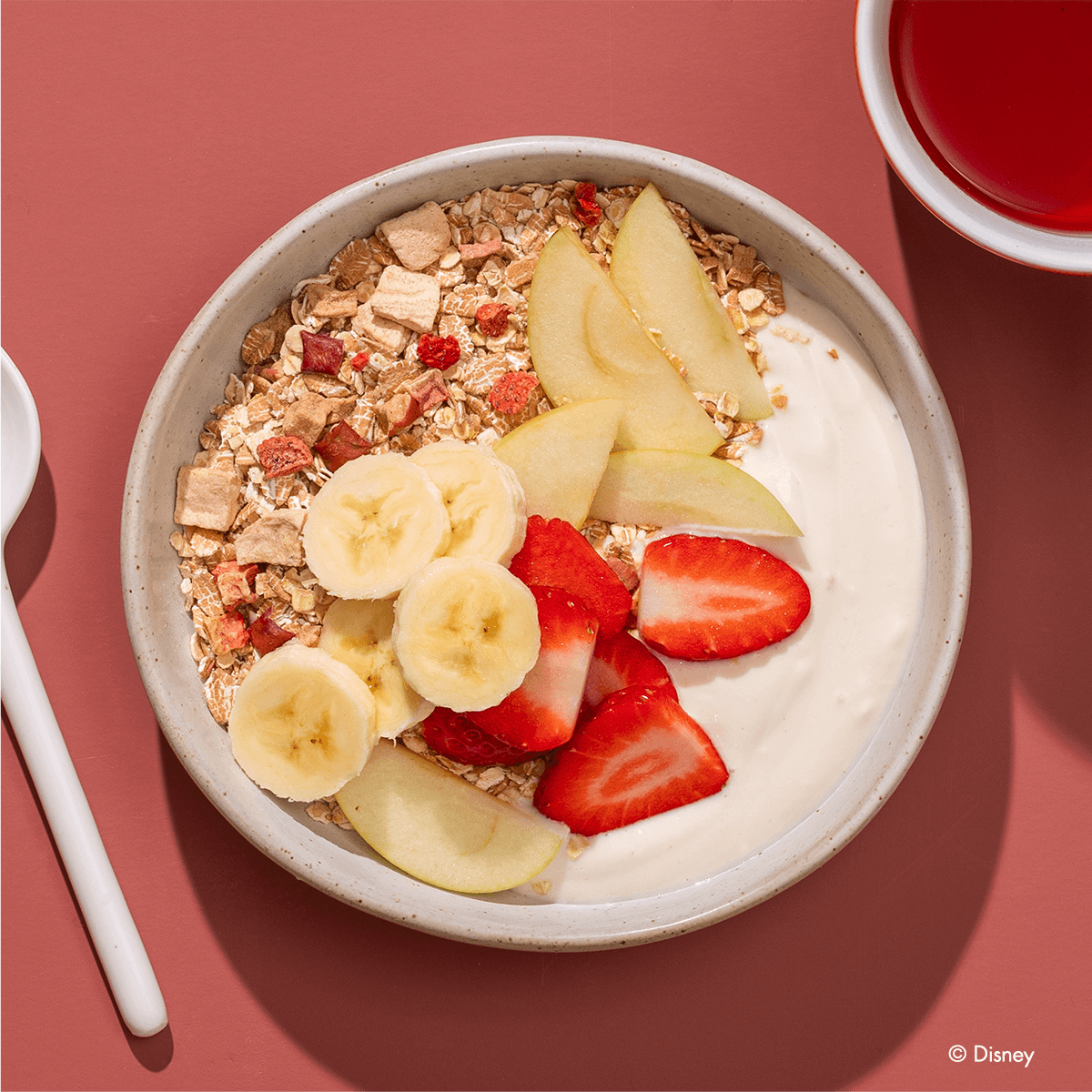 Disney Guten Morgen Löwe Müsli in einer Müslischale mit Bananenscheiben, Erdbeeren, Apfelspalten und Joghurt.