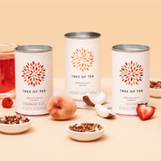 Tree of Tea Bio Früchteteeset mit Red Ruby, Peachy June und Strawberry Bliss Tee neben Teeglas, Pfirsich, Kokosnuss und Erdbeeren