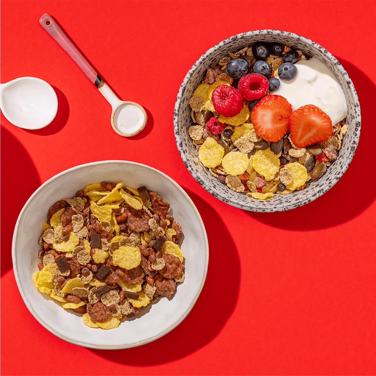 mymuesli Bio Glutenfreies Müsli Probierpaket mit zwei Sorten: Schoko Müsli und Berry Müsli - beide in Schalen gefüllt neben Löffel