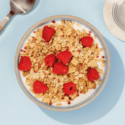 mymuesli Bio Low Sugar Yoghurt Raspberry Crunch in Schale mit Joghurt und frischen Himbeeren
