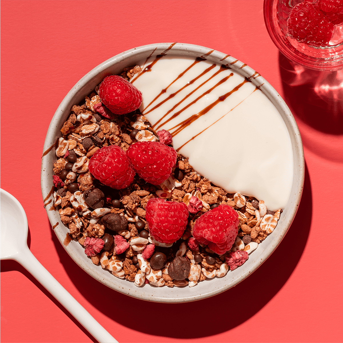 mymuesli Bio Raspberry Dark Choc Müsli in Schüssel mit Joghurt und frischen Himbeeren serviert mit Himbeer Smoothie