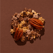 Eine Nahaufnahme der Granola-Mischung auf braunem Grund mit großen Pekannüssen, Knusper-Clustern und Schokoladenstücken.