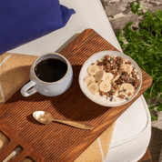 Eine Schale mit Choco Banana Müsli, Joghurt, zwei halbe Bananen und Schokosauce und eine Tasse Kaffee 