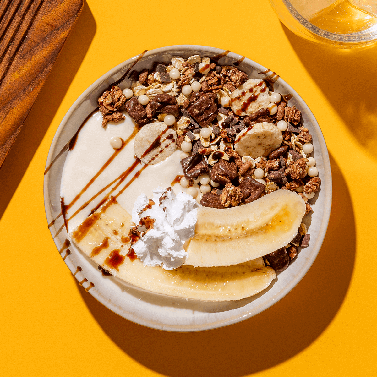 mymuesli Bio Choco Banana Müsli in der Schüssel mit halbierten Bananen, Sahne und Joghurt