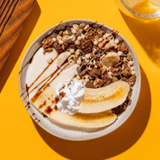 mymuesli Bio Choco Banana Müsli in der Schüssel mit halbierten Bananen, Sahne und Joghurt