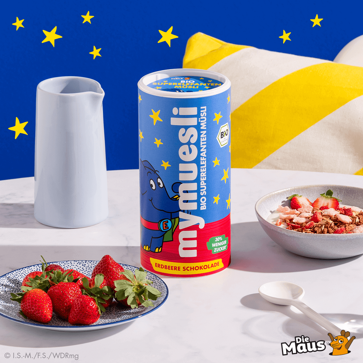 mymuesli Bio Superelefanten Müsli Dose und daneben eine Schale mit Superelefanten Müsli, Joghurt und frischen Erdbeeren
