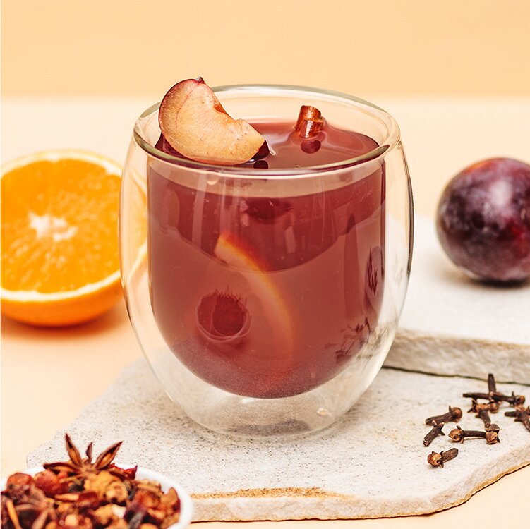 Pflaumen Punsch mit einer halben Orange, Pflaumen, Nelken und Tee daneben