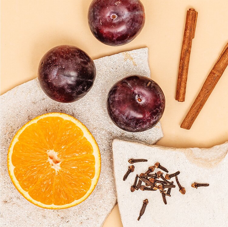 Eine halbe Orange mit Pflaumen, Nelken und Zimtstangen daneben