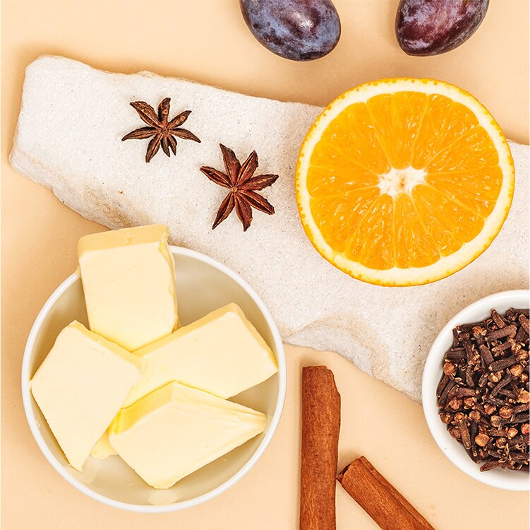 Butter in einer Schale, eine halbe Orange und Gewürze daneben