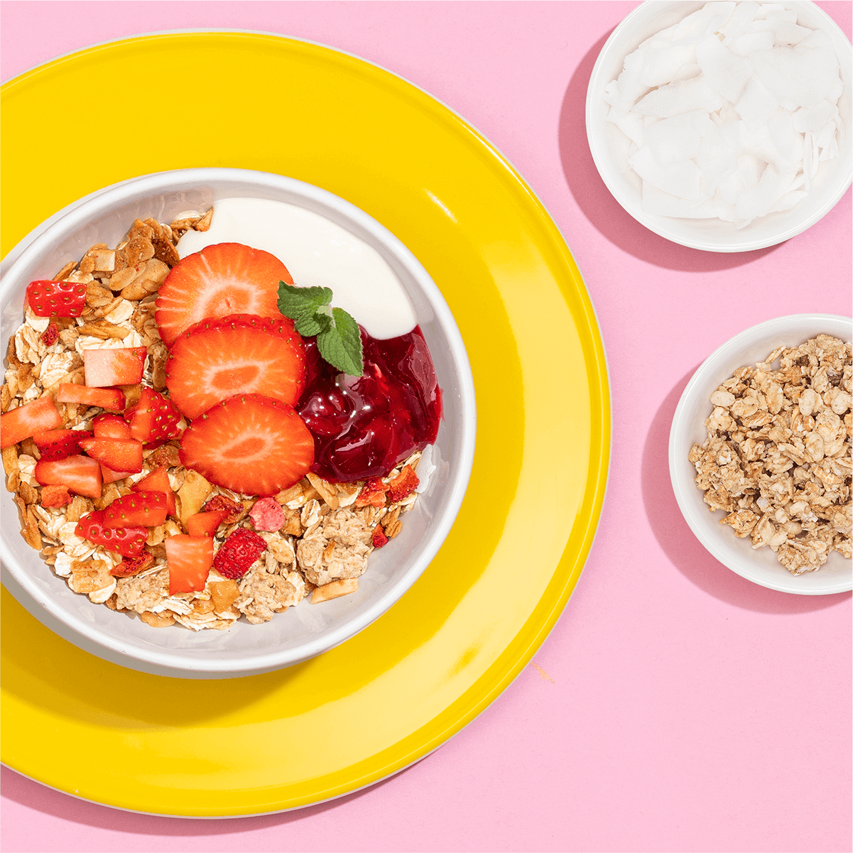 Mueslischale mit Muesli, Erdbeeren und roter Gruetze auf gelb und rosa gestaltetem Tisch