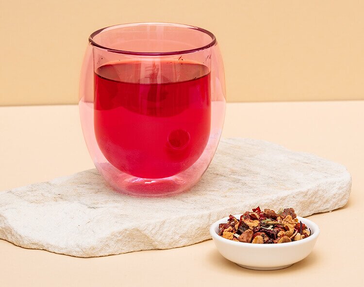 Rosa doppelwandiges Teeglas mit Schwebeeffekt mit rotem Fruechtetee gefuellt